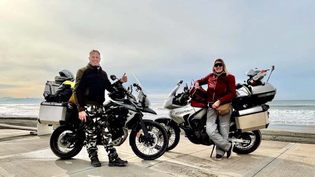 Motociclistas viajando de big trail por paisagem árida e montanhosa no Irã, com um sol forte no horizonte, simbolizando os desafios do mototurismo internacional.