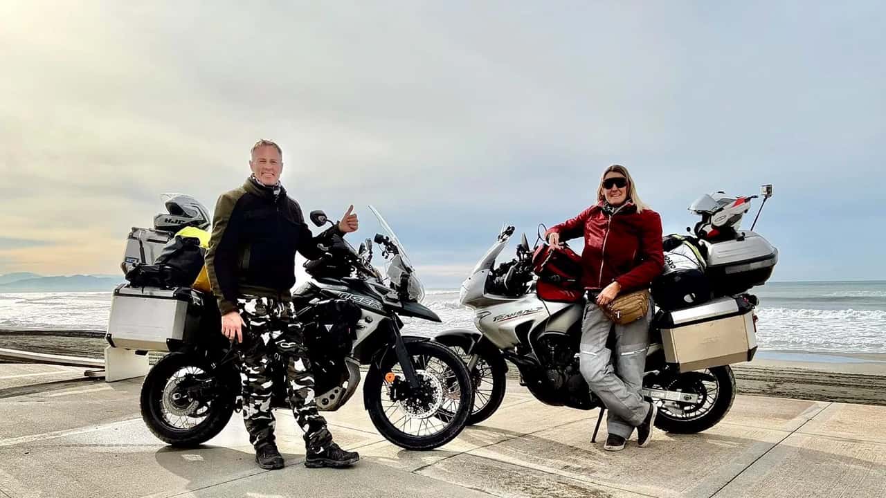 Motociclistas viajando de big trail por paisagem árida e montanhosa no Irã, com um sol forte no horizonte, simbolizando os desafios do mototurismo internacional.