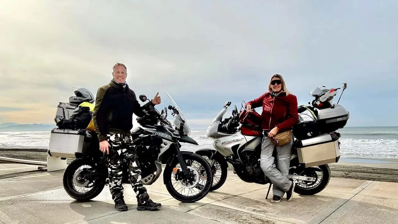 Motociclistas viajando de big trail por paisagem árida e montanhosa no Irã, com um sol forte no horizonte, simbolizando os desafios do mototurismo internacional.