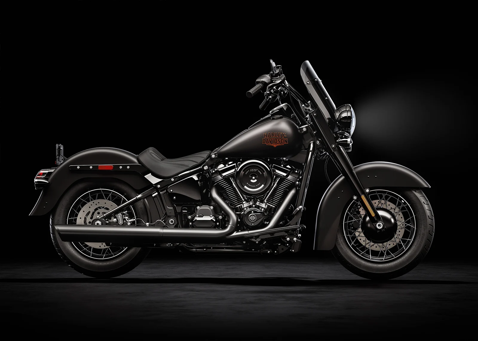 Renderização conceitual de uma motocicleta Harley-Davidson Deadwood estilo bobber retro em uma estrada sinuosa, com farol único e banco solo, em tons escuros e cromados.