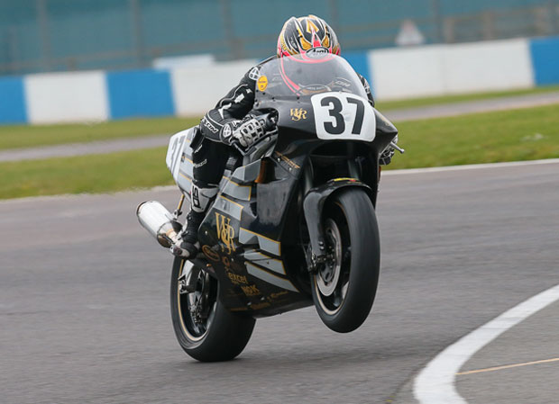 Peter Hickman se preparando para pilotar a lendária moto de corrida Norton Rotary na Snaefell Mountain Course do Classic TT, destacando o motor Wankel e seu design clássico de corrida.