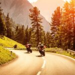 Motociclista com equipamento completo pilotando sua moto em uma estrada ensolarada durante o verão, destacando a importância da segurança