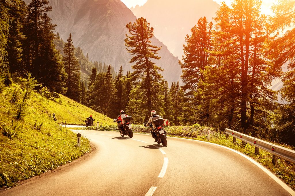 Motociclista com equipamento completo pilotando sua moto em uma estrada ensolarada durante o verão, destacando a importância da segurança