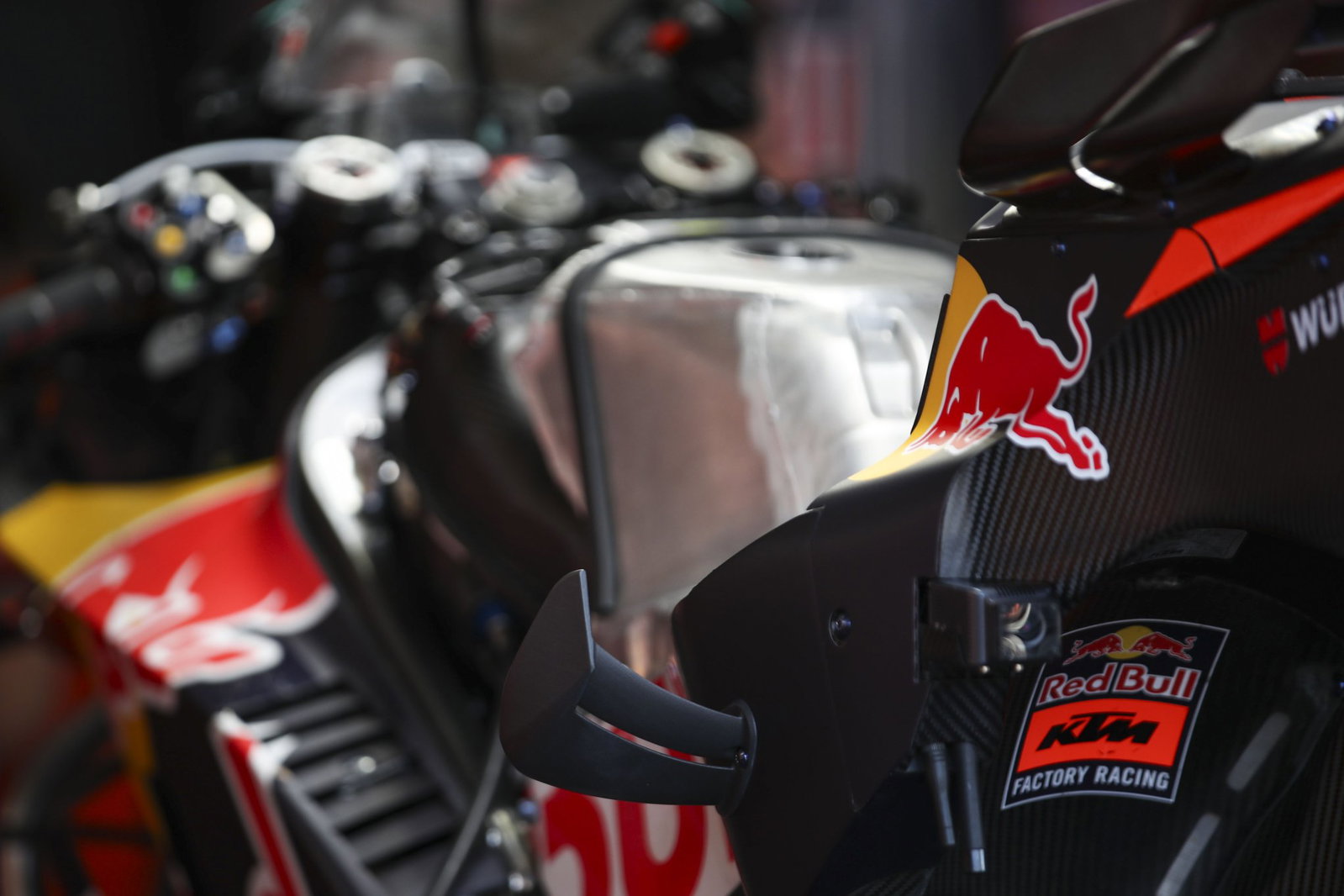 Duas motos KTM RC16 da equipe Red Bull KTM Factory Racing em plena ação na pista de MotoGP, mostrando a potência e a aerodinâmica das máquinas de corrida, mas enfrentando problemas de motor.