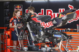 Duas motos KTM RC16 da equipe Red Bull KTM Factory Racing em plena ação na pista de MotoGP, mostrando a potência e a aerodinâmica das máquinas de corrida, mas enfrentando problemas de motor.