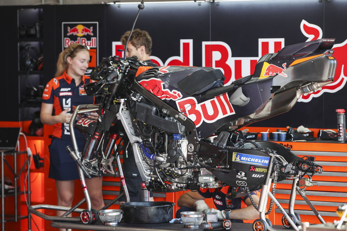 Duas motos KTM RC16 da equipe Red Bull KTM Factory Racing em plena ação na pista de MotoGP, mostrando a potência e a aerodinâmica das máquinas de corrida, mas enfrentando problemas de motor.