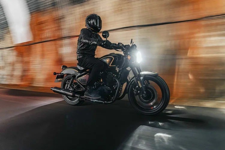 Royal Enfield Shotgun 650 x Rough Crafts, uma motocicleta customizada em preto fosco com detalhes dourados e componentes artesanais, exibida em um fundo escuro.
