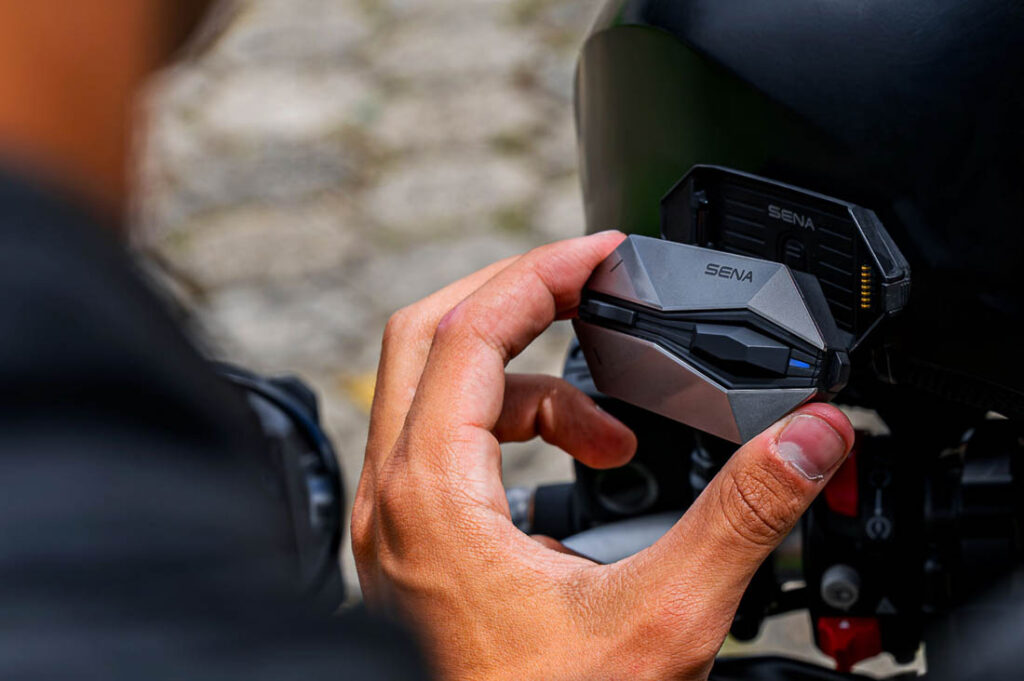 Imagem de um motociclista utilizando o Sena 60X intercomunicador em seu capacete, destacando o novo design e o joystick intuitivo para comunicação avançada em viagens.