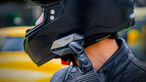 Imagem de um motociclista utilizando o Sena 60X intercomunicador em seu capacete, destacando o novo design e o joystick intuitivo para comunicação avançada em viagens.