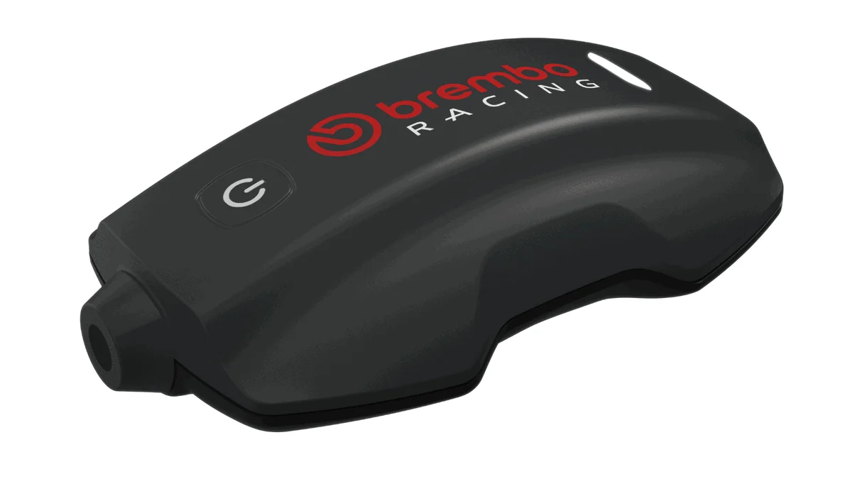 Sistema Brembo TrackTribe sendo exibido, destacando sua interface digital e o prestigioso troféu Red Dot Award, simbolizando a inovação em monitoramento de dados para motociclismo.