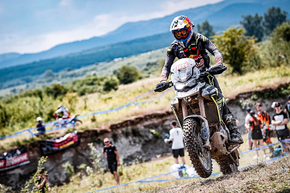 Uma Triumph Tiger 900 Rally Pro em ação em uma trilha técnica de hard enduro, com um piloto experiente. Foco na robustez da motocicleta.