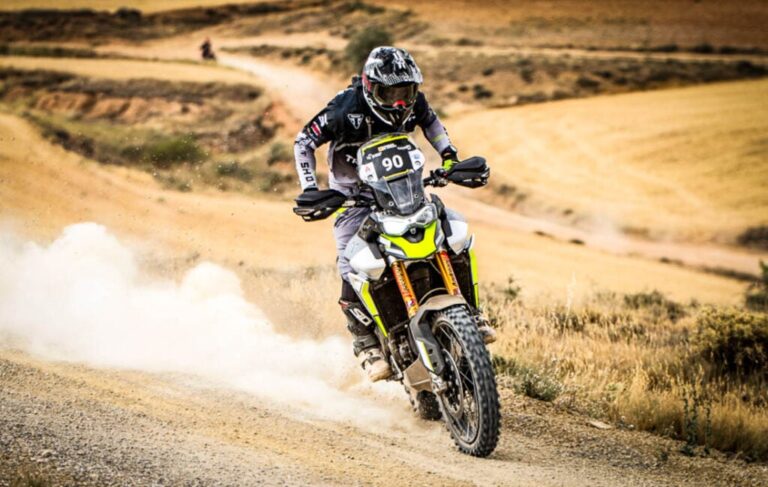 Uma Triumph Tiger 900 Rally Pro em ação em uma trilha técnica de hard enduro, com um piloto experiente. Foco na robustez da motocicleta.