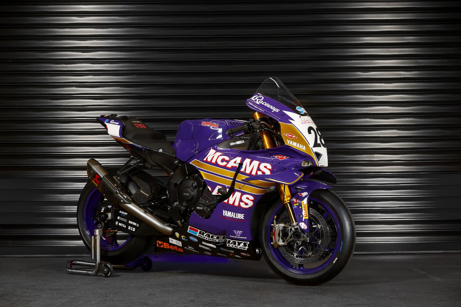 Uma moto de corrida Yamaha YZF-R1 com a icônica pintura roxa e laranja da Cadbury's Boost, pilotada por James Haydon, em alta velocidade na pista do Campeonato Britânico de Superbike (BSB), evocando nostalgia.