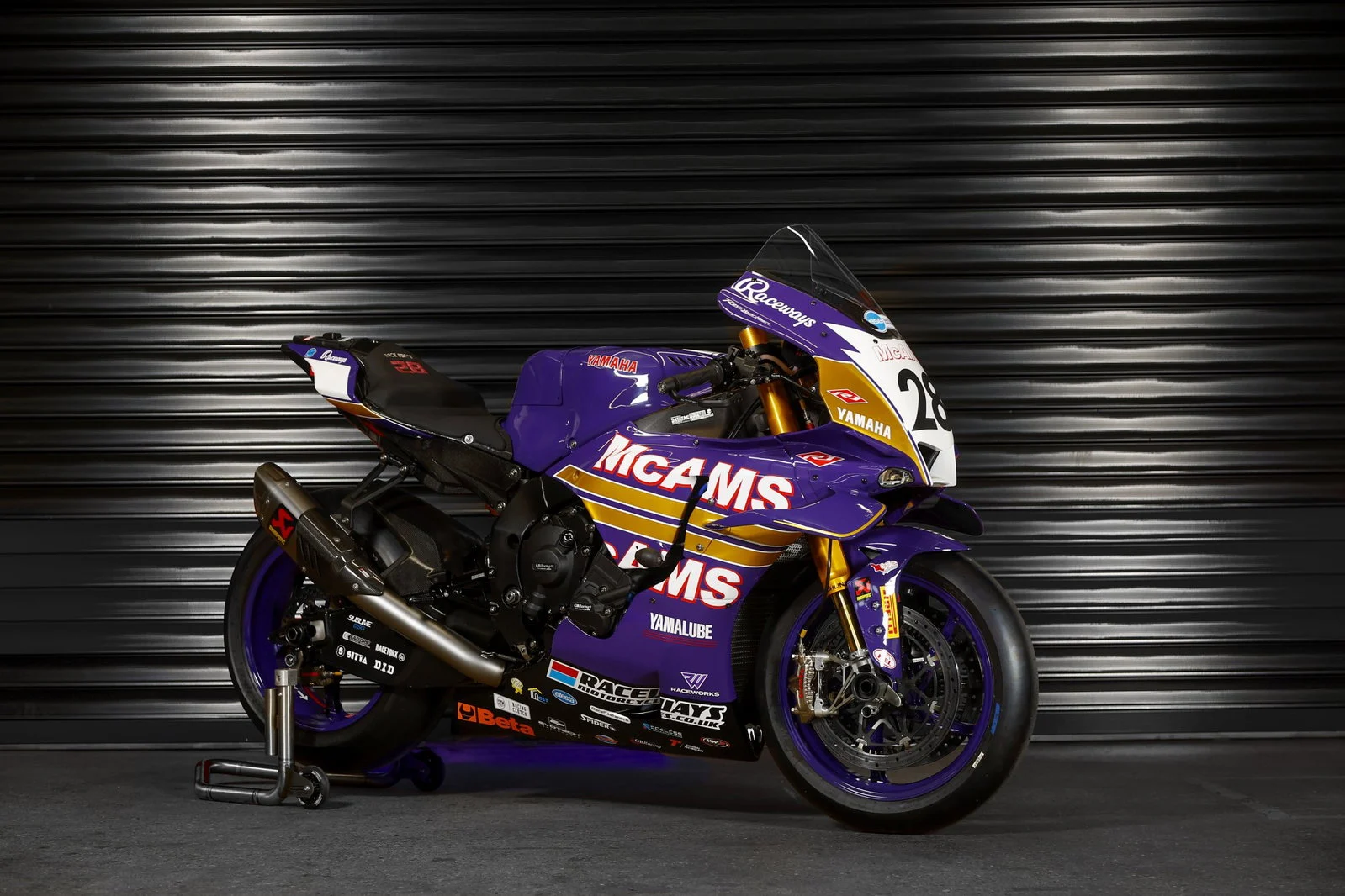 Uma moto de corrida Yamaha YZF-R1 com a icônica pintura roxa e laranja da Cadbury's Boost, pilotada por James Haydon, em alta velocidade na pista do Campeonato Britânico de Superbike (BSB), evocando nostalgia.