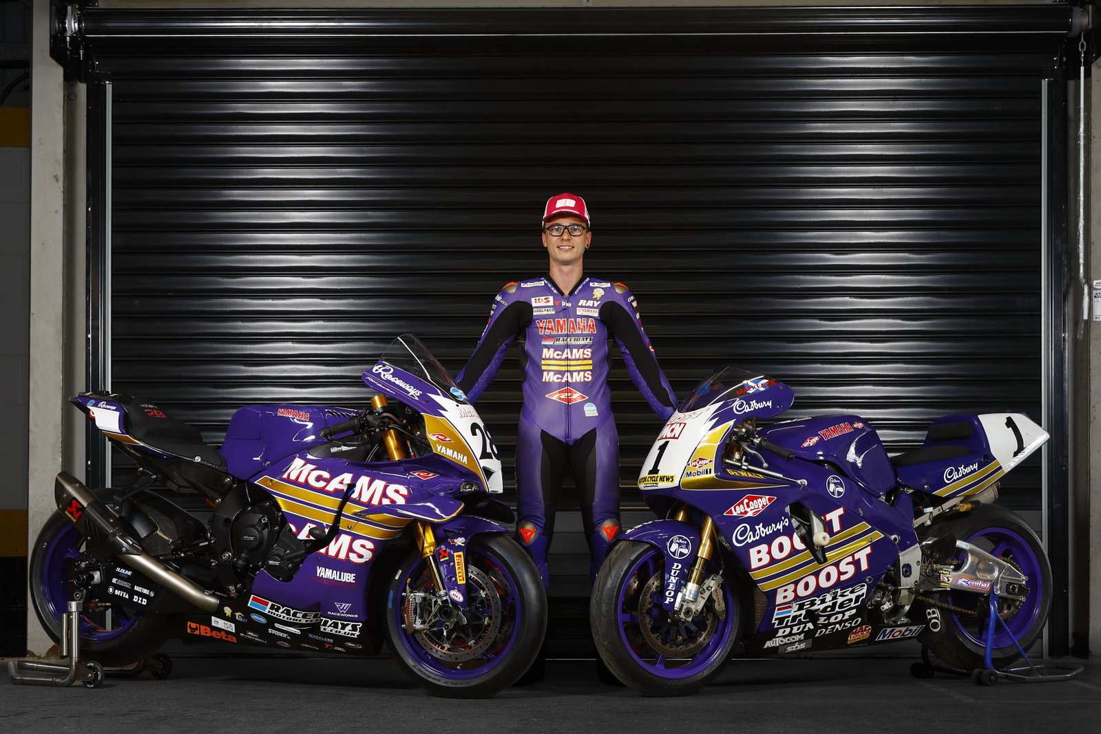 Uma moto de corrida Yamaha YZF-R1 com a icônica pintura roxa e laranja da Cadbury's Boost, pilotada por James Haydon, em alta velocidade na pista do Campeonato Britânico de Superbike (BSB), evocando nostalgia.
