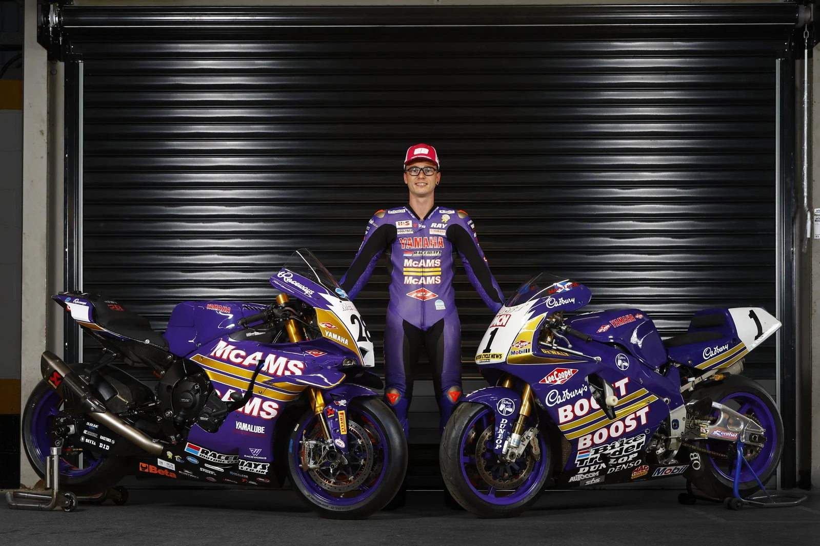 Uma moto de corrida Yamaha YZF-R1 com a icônica pintura roxa e laranja da Cadbury's Boost, pilotada por James Haydon, em alta velocidade na pista do Campeonato Britânico de Superbike (BSB), evocando nostalgia.
