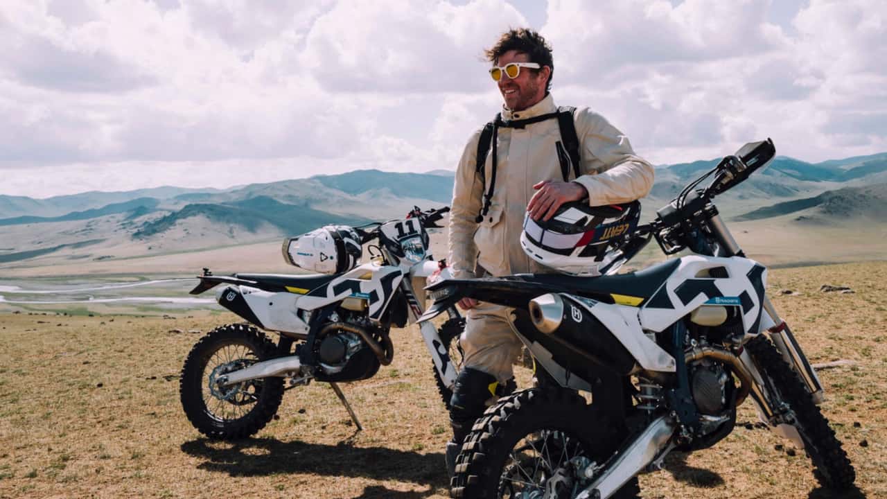 Norman Reedus em sua motocicleta de aventura, vestido com equipamento ADV da Aether, explorando paisagens remotas na Mongólia, sob um céu dramático.