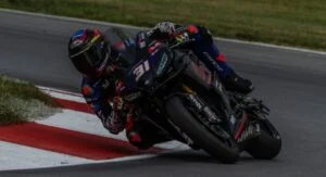 Hank Vossberg pilotando a Aprilia RS 660 em alta velocidade na pista de Mid-Ohio durante a competição da Twins Cup no MotoAmerica, em uma curva acentuada com outros competidores ao fundo.