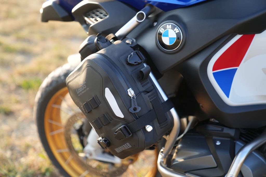 Bolsa Loboo Wanderer de cor preta fixada em uma barra de proteção de uma motocicleta de aventura, destacando sua integração com a estrutura da moto.