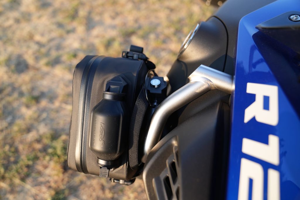 Bolsa Loboo Wanderer de cor preta fixada em uma barra de proteção de uma motocicleta de aventura, destacando sua integração com a estrutura da moto.