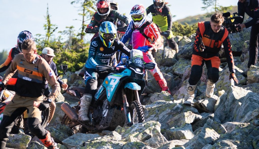 CFMOTO 450MT em ação superando obstáculos extremos em uma trilha de hard enduro na Red Bull Romaniacs, com paisagem montanhosa ao fundo.