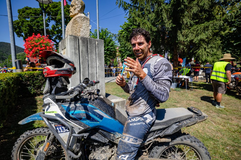 CFMOTO 450MT em ação superando obstáculos extremos em uma trilha de hard enduro na Red Bull Romaniacs, com paisagem montanhosa ao fundo.
