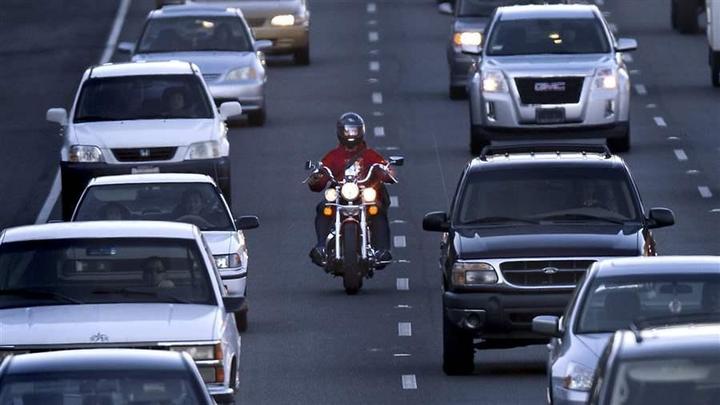 Motociclista navegando com segurança entre carros parados em um engarrafamento urbano, praticando o lane splitting ou corredor de forma atenta e legal.