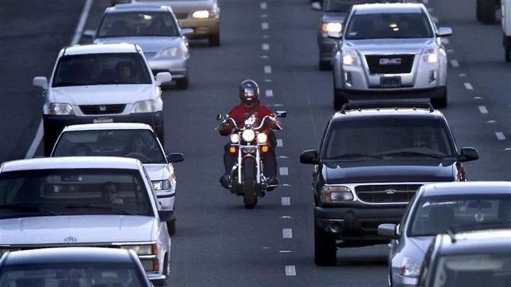 Motociclista navegando com segurança entre carros parados em um engarrafamento urbano, praticando o lane splitting ou corredor de forma atenta e legal.