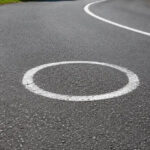 Círculos brancos pintados no asfalto de uma estrada sinuosa na Espanha, visando melhorar a trajetória e a segurança de motociclistas em curvas perigosas.