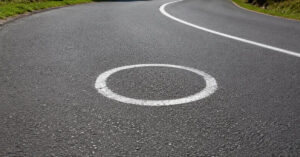 Círculos brancos pintados no asfalto de uma estrada sinuosa na Espanha, visando melhorar a trajetória e a segurança de motociclistas em curvas perigosas.