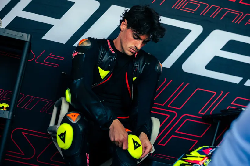 Valentino Rossi e outros pilotos de MotoGP ao lado de engenheiros da Dainese, analisando um macacão de segurança no circuito de Misano durante o Project Apex 2026.