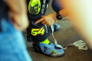 Valentino Rossi e outros pilotos de MotoGP ao lado de engenheiros da Dainese, analisando um macacão de segurança no circuito de Misano durante o Project Apex 2026.