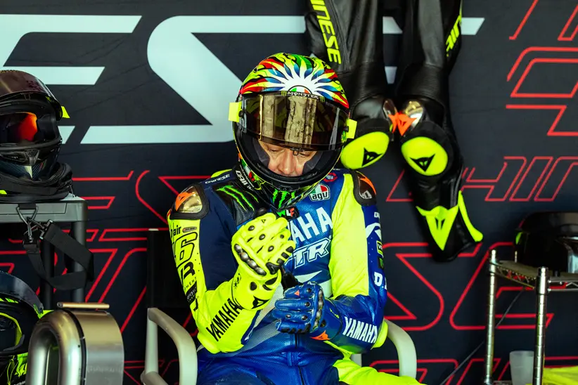 Valentino Rossi e outros pilotos de MotoGP ao lado de engenheiros da Dainese, analisando um macacão de segurança no circuito de Misano durante o Project Apex 2026.