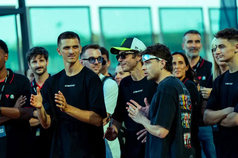 Valentino Rossi e outros pilotos de MotoGP ao lado de engenheiros da Dainese, analisando um macacão de segurança no circuito de Misano durante o Project Apex 2026.