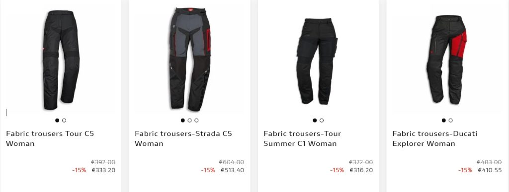 Motociclista vestindo equipamento completo Ducati, incluindo calças e botas, em uma moto esportiva na estrada.