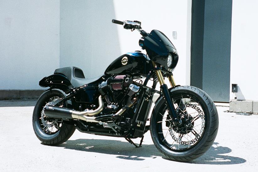 Harley-Davidson Street Bob personalizada no estilo Clubstyle, em tons escuros e com guidão alto, exibindo detalhes em homenagem a Chester Bennington, em um cenário urbano noturno.