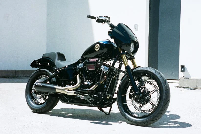 Harley-Davidson Street Bob personalizada no estilo Clubstyle, em tons escuros e com guidão alto, exibindo detalhes em homenagem a Chester Bennington, em um cenário urbano noturno.