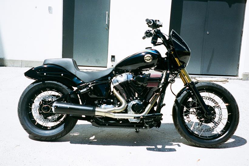 Harley-Davidson Street Bob personalizada no estilo Clubstyle, em tons escuros e com guidão alto, exibindo detalhes em homenagem a Chester Bennington, em um cenário urbano noturno.