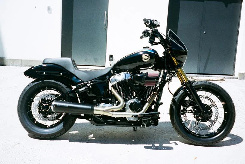 Harley-Davidson Street Bob personalizada no estilo Clubstyle, em tons escuros e com guidão alto, exibindo detalhes em homenagem a Chester Bennington, em um cenário urbano noturno.