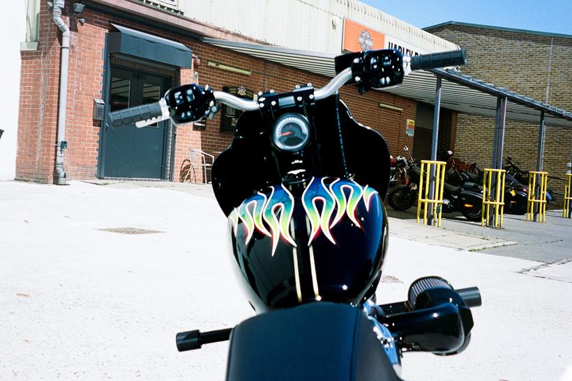 Harley-Davidson Street Bob personalizada no estilo Clubstyle, em tons escuros e com guidão alto, exibindo detalhes em homenagem a Chester Bennington, em um cenário urbano noturno.