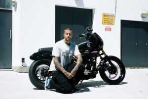 Harley-Davidson Street Bob personalizada no estilo Clubstyle, em tons escuros e com guidão alto, exibindo detalhes em homenagem a Chester Bennington, em um cenário urbano noturno.