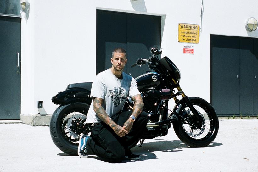 Harley-Davidson Street Bob personalizada no estilo Clubstyle, em tons escuros e com guidão alto, exibindo detalhes em homenagem a Chester Bennington, em um cenário urbano noturno.