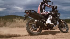 Motociclistas do Honda Adventure Roads 2026 pilotando a Honda XL750 Transalp por uma estrada sinuosa e cênica nas montanhas dos Pirenéus, com picos nevados ao fundo e céu azul.