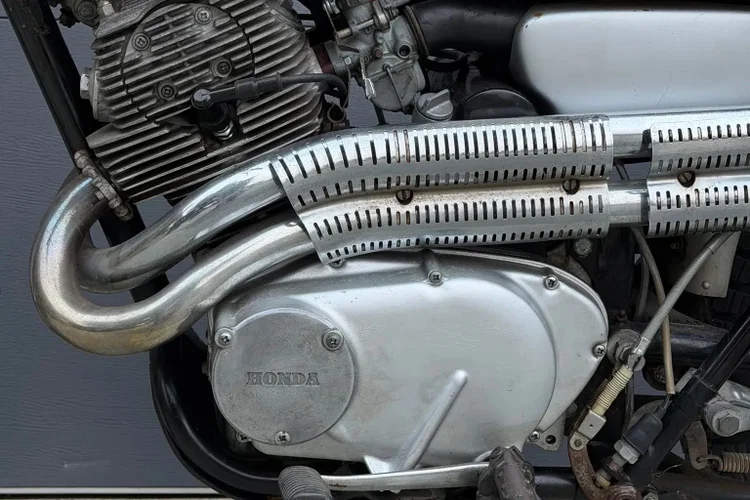 Honda CL72 Scrambler de 1964, modelo associado a Elvis Presley, exibida em leilão com detalhes do seu design clássico e motor. Ilustração da moto no contexto de um evento de leilão de veículos antigos.