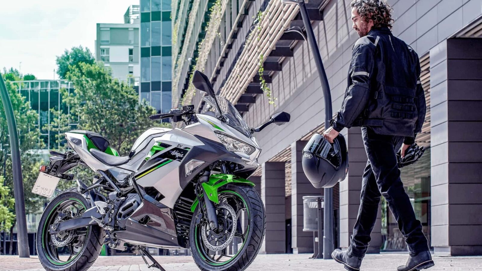 Uma Kawasaki Ninja e-1 na cor verde limão e preta, com design esportivo característico da linha Ninja, estacionada em um ambiente urbano. Destaca a carenagem aerodinâmica e os detalhes elétricos do modelo de 2027.