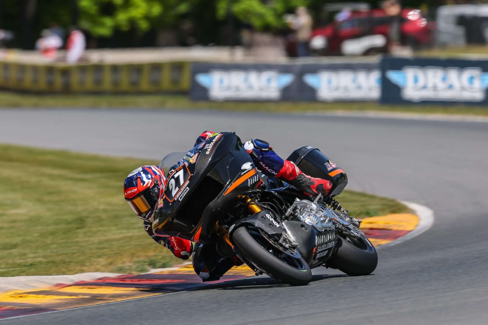 Max Toth pilotando uma motocicleta Harley-Davidson Bagger em alta velocidade durante uma corrida, com a pista de Silverstone ao fundo, ilustrando a competição do Bagger World Cup.