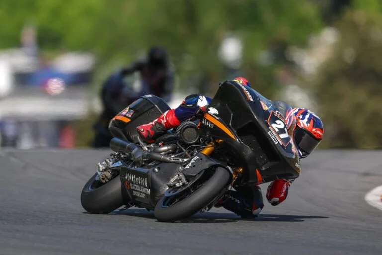 Max Toth pilotando uma motocicleta Harley-Davidson Bagger em alta velocidade durante uma corrida, com a pista de Silverstone ao fundo, ilustrando a competição do Bagger World Cup.