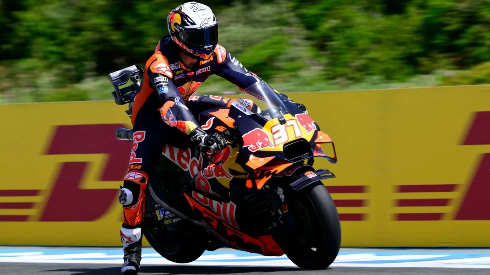 Motos KTM RC16 competindo em alta velocidade na pista de MotoGP, com a equipe trabalhando nos boxes