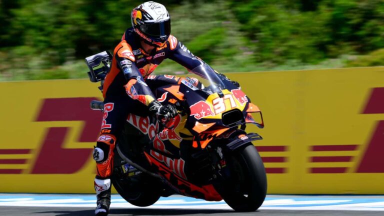 Motos KTM RC16 competindo em alta velocidade na pista de MotoGP, com a equipe trabalhando nos boxes