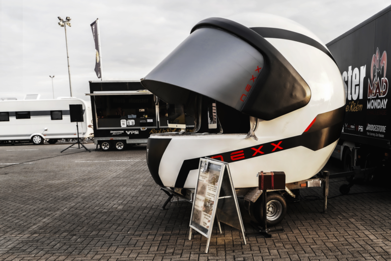 Capacete gigante NEXX sendo transportado por uma estrada europeia, simbolizando a jornada e a aventura do motociclismo.